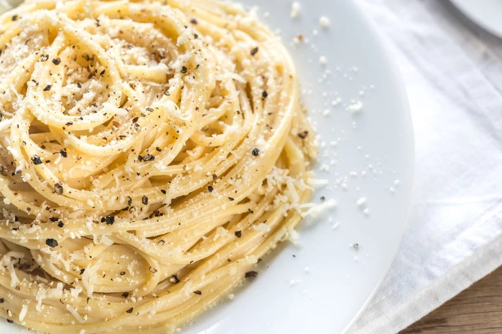 Porcja spaghetti z tartym parmezanem i świeżo mielonym czarnym pieprzem na białym talerzu