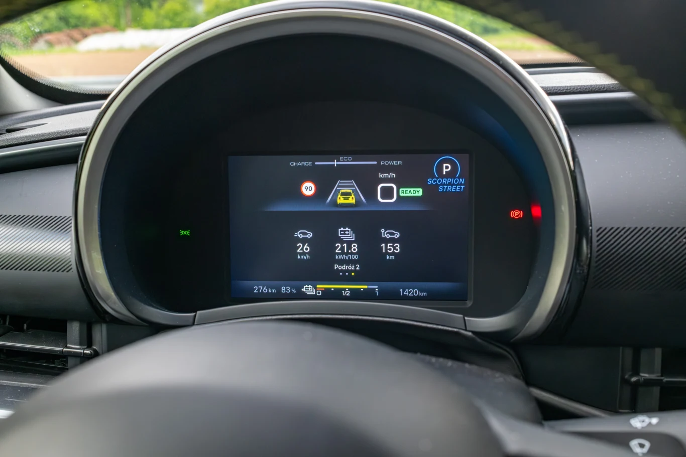 Cyfrowy wyświetlacz kokpitu samochodu elektrycznego z widocznymi wskaźnikami poziomu naładowania, zasięgu, prędkości oraz ikonami ostrzegawczymi i informacyjnymi