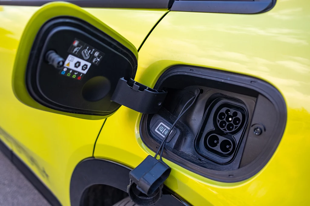 600e można ładować prądem o mocy 100 kW Klapka wlewu i gniazdo ładowania elektrycznego samochodu w jasnożółtym kolorze, wyeksponowana instalacja przygotowana do podłączenia kabla.