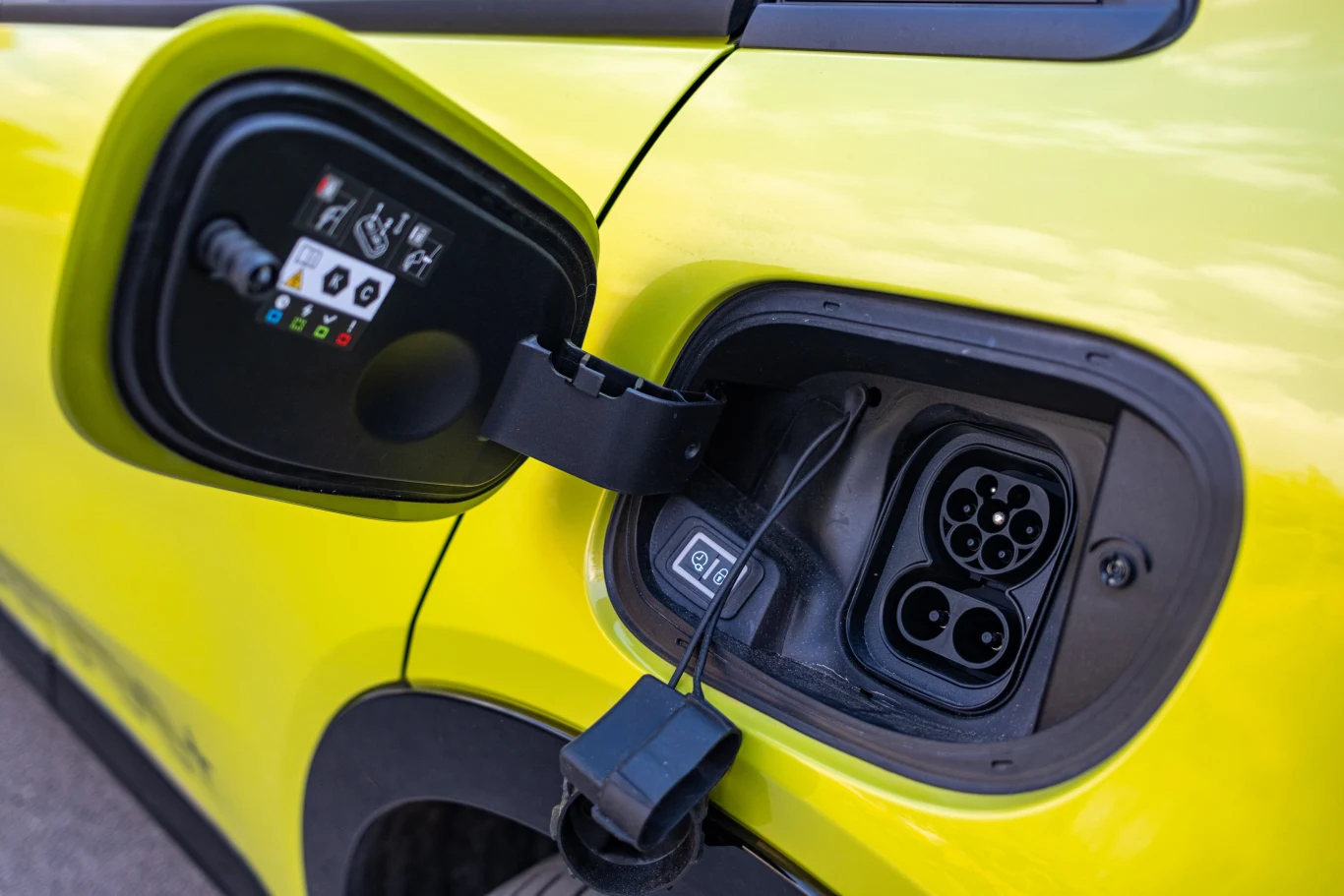 Klapka wlewu i gniazdo ładowania elektrycznego samochodu w jasnożółtym kolorze, wyeksponowana instalacja przygotowana do podłączenia kabla.