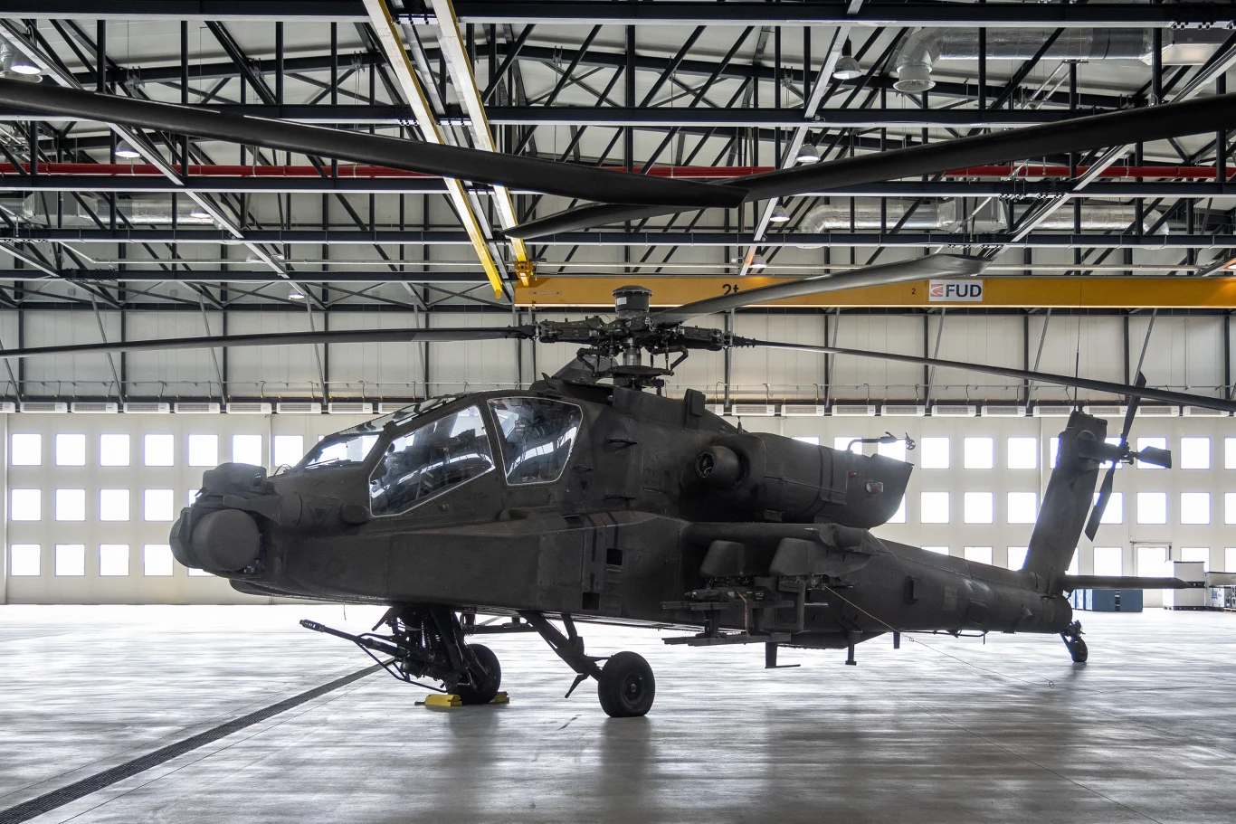 AH-64D w 56. Bazie Lotniczej pod Inowrocławiem. Śmigłowiec bojowy AH-64 Apache ustawiony w hangarze, dobrze widoczne wirniki, kokpit oraz uzbrojenie zamontowane pod skrzydłami, całość wnętrza hangaru z dużymi oknami w tle.