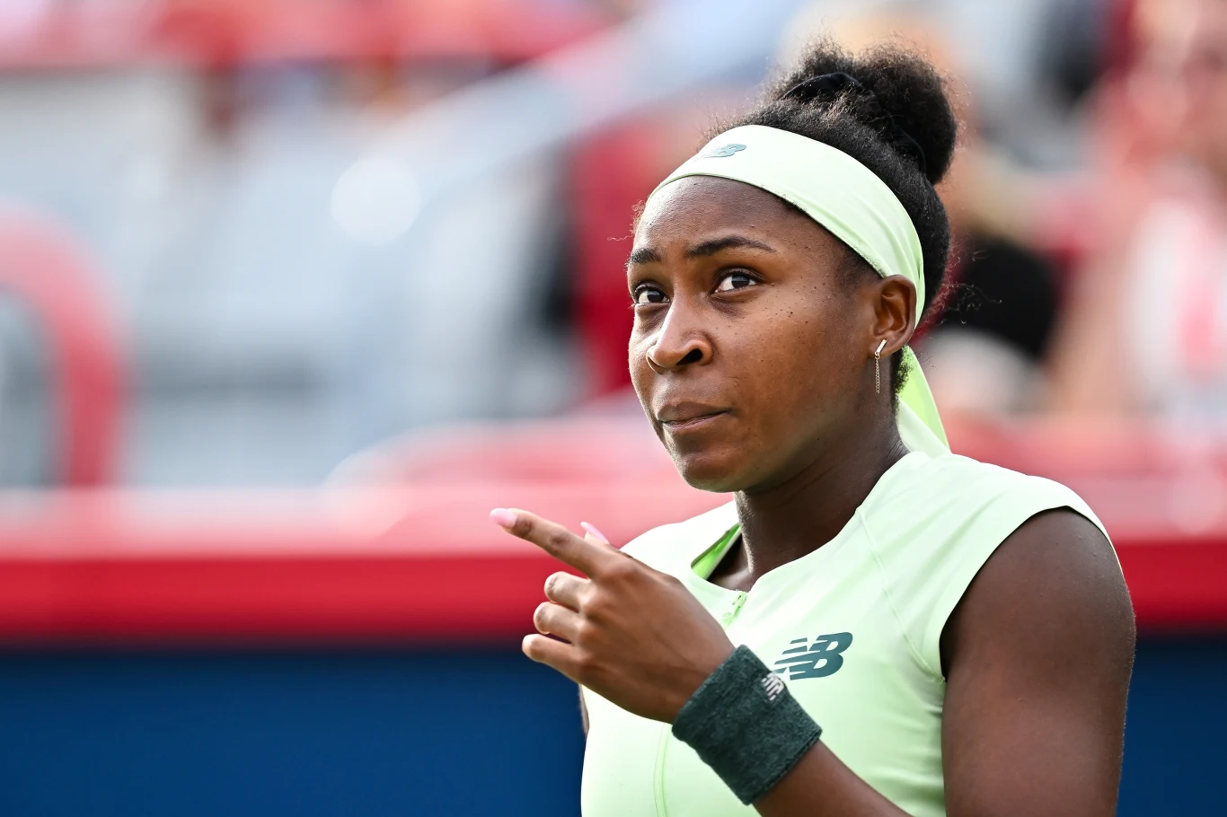 Młoda sportsmenka w jasnozielonym stroju tenisowym i opasce na głowie stoi na korcie, patrząc z determinacją w stronę obiektywu i wskazując palcem.