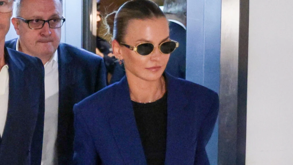 Anna Lewandowska Kobieta w okularach przeciwsłonecznych i granatowej marynarce stoi obok mężczyzny w garniturze, oboje wchodzą przez drzwi, tło rozmyte