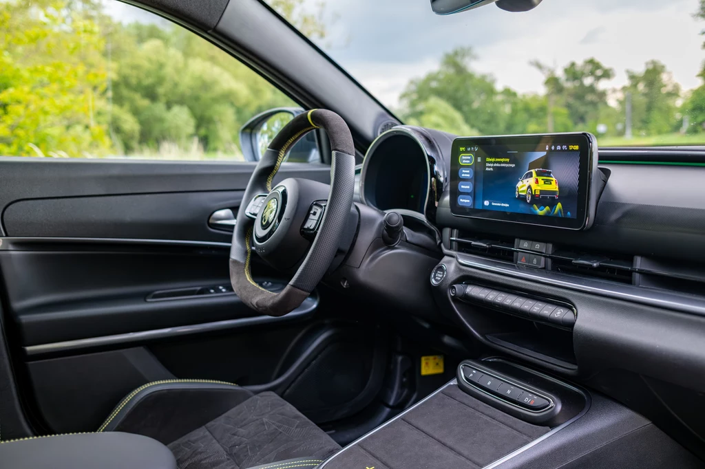 Abarth 600e Scorpionissima Wnętrze nowoczesnego samochodu osobowego z cyfrowym panelem sterowania na kokpicie, multifunkcyjną kierownicą oraz rozbudowanym systemem multimedialnym z wyświetlaczem dotykowym ukazującym interfejs pojazdu