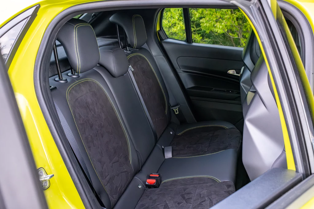 Abarth 600e Scorpionissima Wnętrze tylnej części samochodu osobowego z czarnymi, tekstylnymi siedzeniami, żółtym nadwoziem i widokiem na zieleń za oknem.