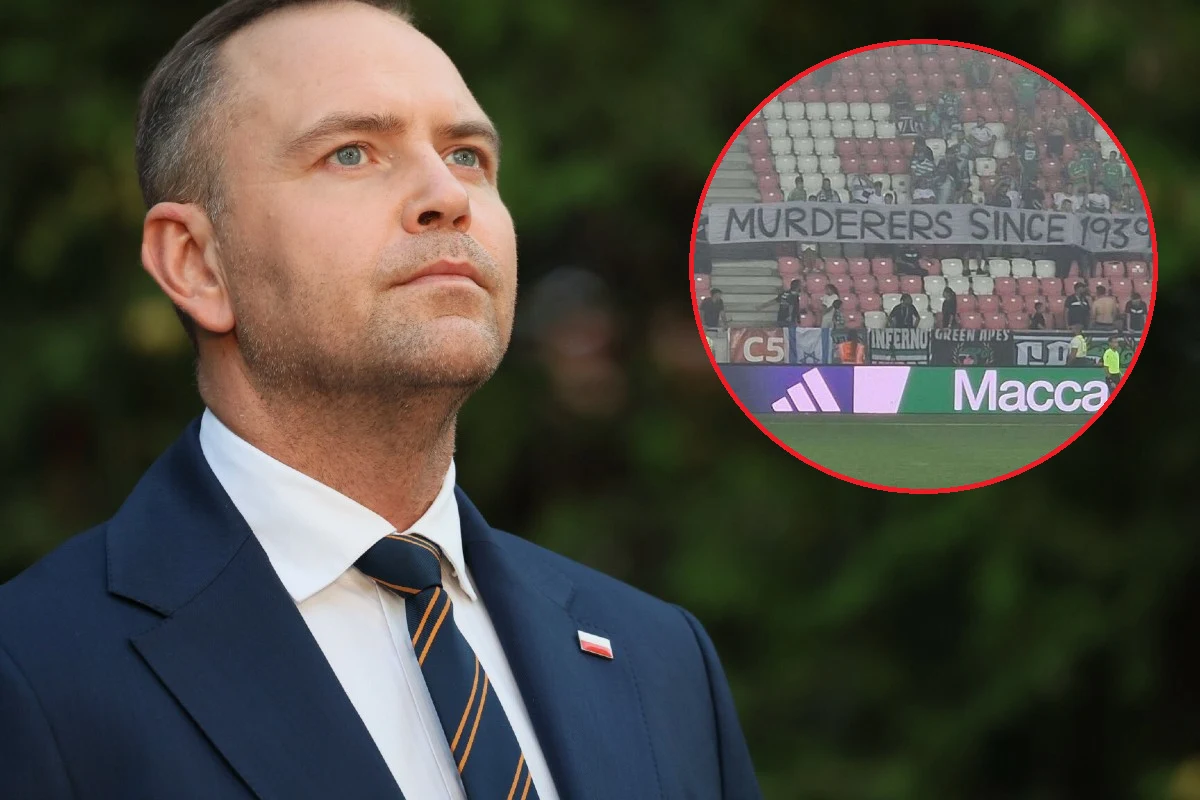 Mężczyzna w garniturze z przypiętą flagą Polski na klapie, w tle powiększone ujęcie fragmentu stadionu z banerem zawierającym obraźliwy angielski napis.