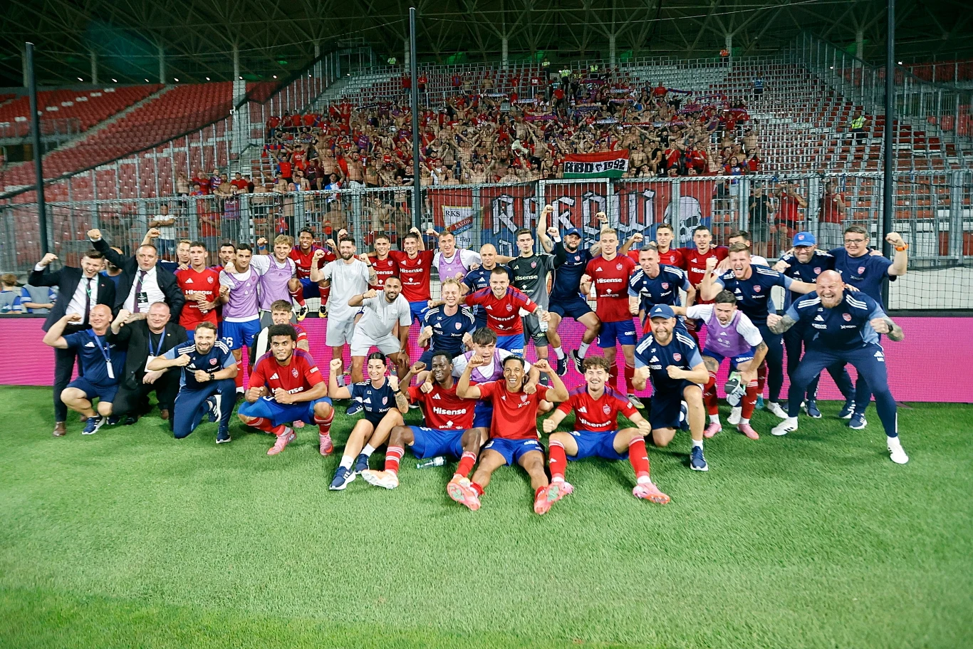 Raków jest na dobrej drodze, aby awansować do fazy ligowej Ligi Konferencji Drużyna piłkarska po zwycięstwie pozuje do wspólnego zdjęcia na murawie stadionu, za nimi widać trybuny wypełnione kibicami cieszącymi się i machającymi flagami.