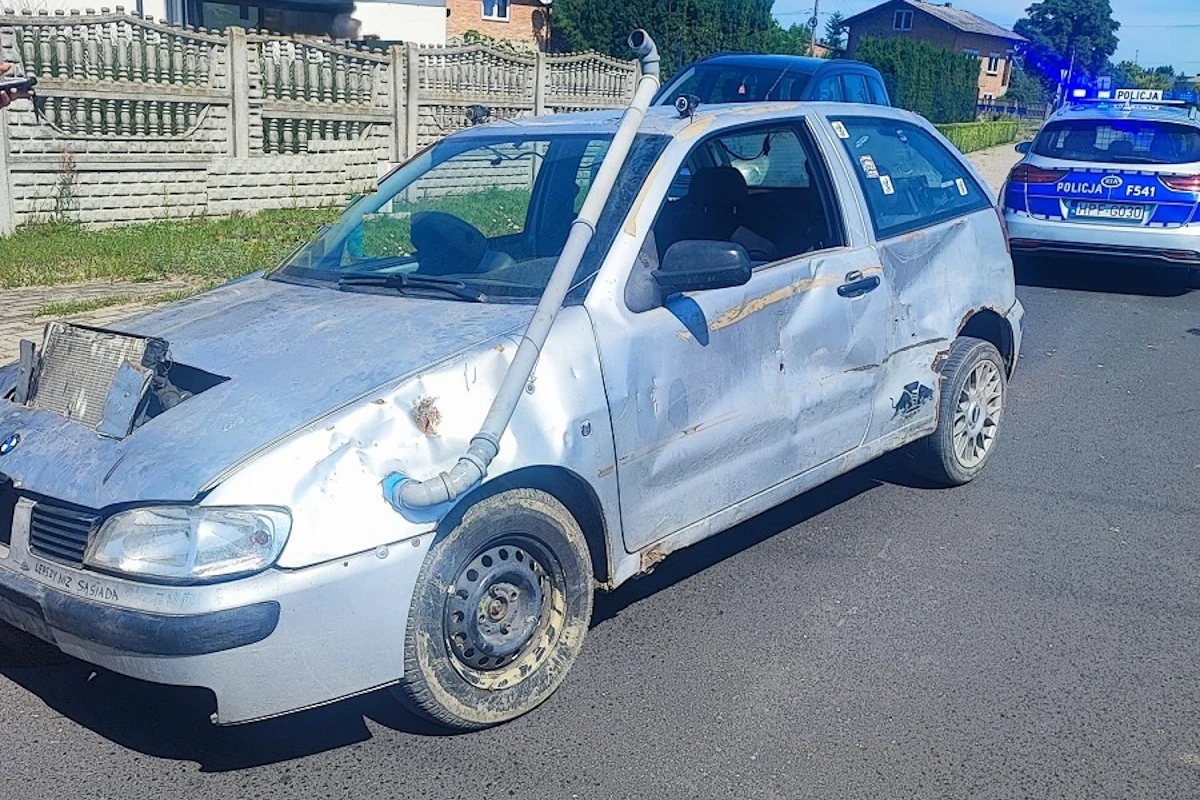 Samochód na zdjęciu to nie tylko wrak, ale obiekt wielu przeróbek. Uwagę przyciąga tzw. snorkel, czyli umieszczony przy dachu chwyt powietrza do silnika Zniszczony samochód osobowy z widocznymi uszkodzeniami karoserii i prowizorycznym wydechem zamontowanym na masce, stojący na drodze; w tle policyjny radiowóz z włączonymi światłami oraz fragment ogrodzenia i domy mieszkalne.