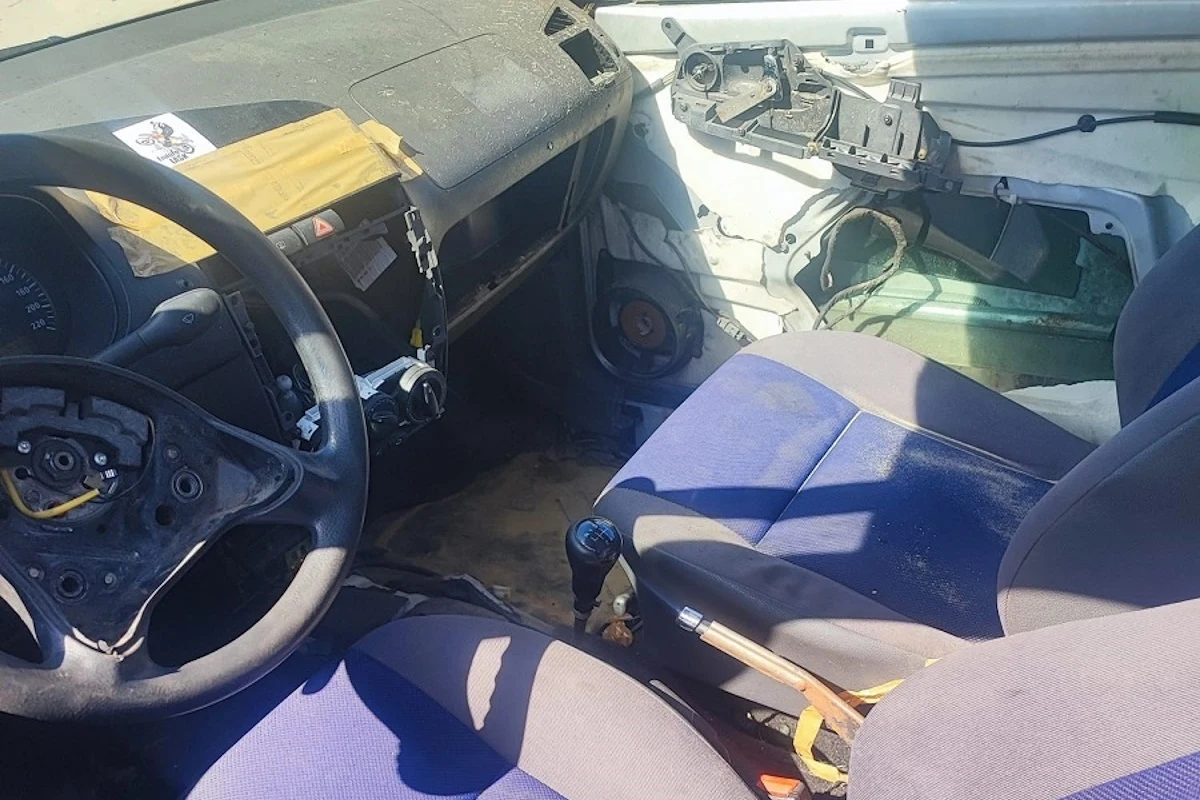 Z kabiny usunięto wszystkie elementy, które nie były konieczne do jazdy Wnętrze zniszczonego samochodu z widocznym brakiem kierownicy, uszkodzoną deską rozdzielczą, brakiem elementów wykończeniowych na drzwiach pasażera i widoczną taśmą naprawczą na kokpicie.