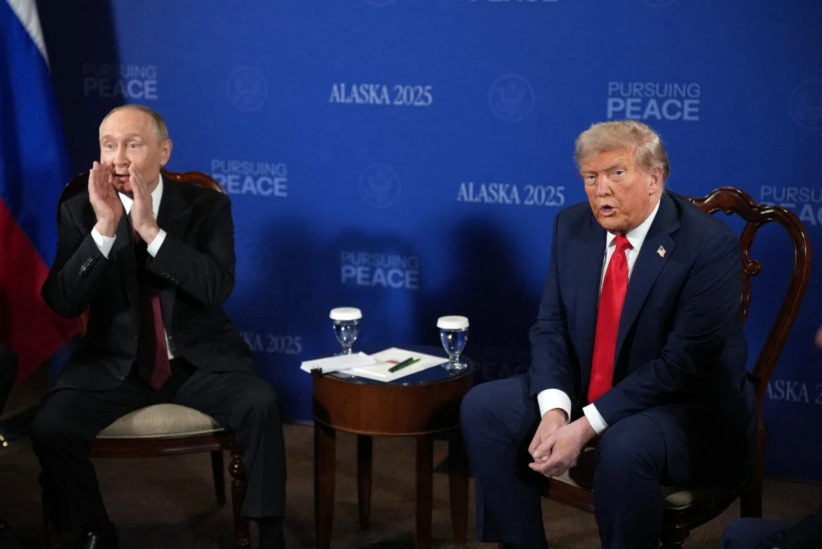 Rozpoczęło się spotkanie Donalda Trumpa z Władimirem Putinem Dwóch mężczyzn siedzi na krzesłach przed niebieskim tłem z napisami 'ALASKA 2025' oraz 'Pursuing Peace', jeden z nich ma gest dłoni przy ustach jakby coś mówił głośno, drugi patrzy prosto przed siebie, na stole pomiędzy nimi znajdują się szklanki z wod...