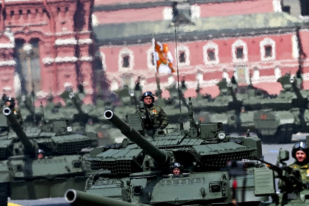 Moskwa ma wkrótce przetestować nowy pocisk Kolumna nowoczesnych czołgów przemieszczająca się przez miasto, w tle historyczna architektura i budynki, żołnierze na wierzchu pojazdów, widoczna flaga oraz duża liczba wojskowych w szyku paradnym.