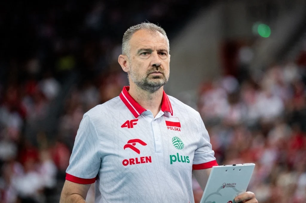 Nikola Grbić skreślił dwóch siatkarzy przed MŚ Mężczyzna w koszulce z napisem Polska i logotypami sponsorów trzyma tablet, stoi na tle rozmytej widowni podczas sportowego wydarzenia.