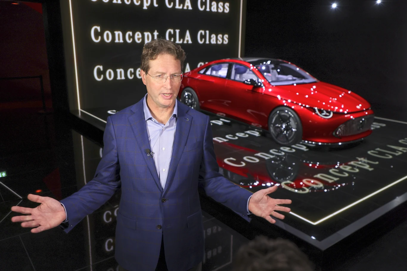 Prezes Mercedesa nie gryzł się w język w kwestii zakazu rejestracji aut spalinowych Mężczyzna w garniturze prezentujący czerwony samochód koncepcyjny Mercedes-Benz CLA Class na futurystycznie zaaranżowanej scenie, z podświetlonym napisem Concept CLA Class w tle.