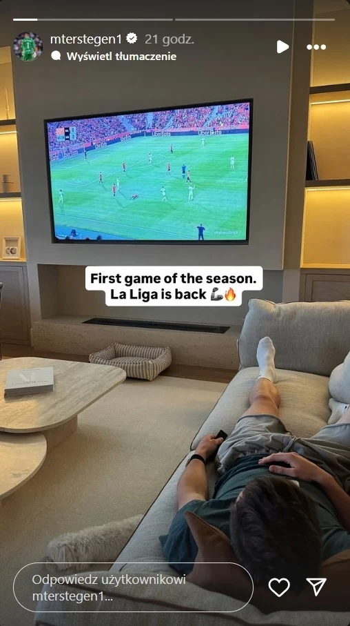 Marc-Andre ter Stegen kibicujący Barcelonie Osoba leżąca na kanapie w nowoczesnym salonie ogląda mecz piłki nożnej na dużym płaskim telewizorze zawieszonym na ścianie, otoczenie jasne i schludne, na stoliku leży kilka przedmiotów codziennego użytku.
