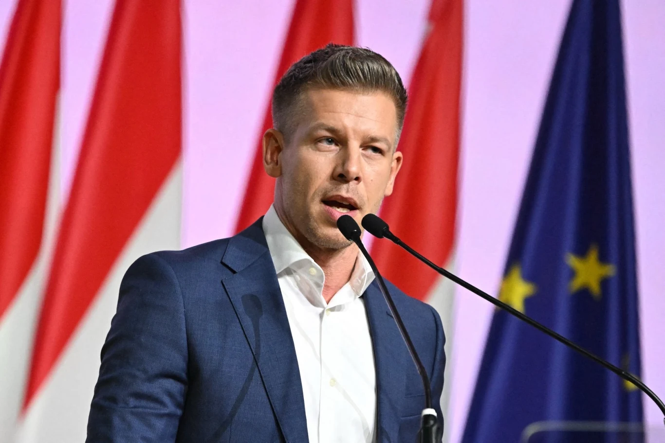 Peter Magyar, lider partii TISZA i przyszły premier Węgier Mężczyzna w garniturze wygłaszający przemówienie przed mikrofonami, w tle widoczne flagi narodowe oraz flaga Unii Europejskiej.