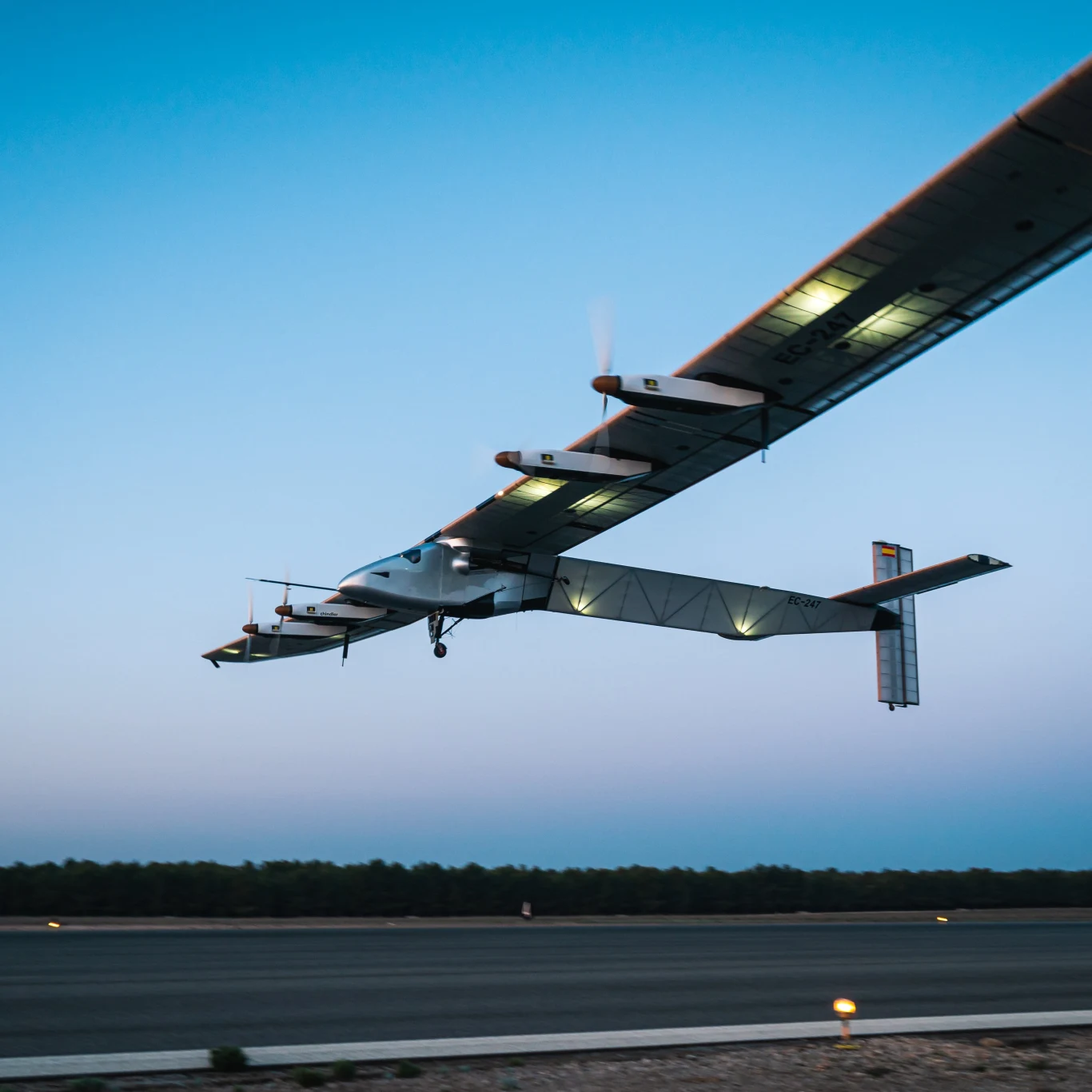 Dron solarny Skydweller Aero jest ogromny i ma rozpiętość skrzydeł większą niż Boeing 747. Eksperymentalny samolot o dużej rozpiętości skrzydeł i nowoczesnej konstrukcji unosi się nad pasem startowym tuż po starcie, przy jasnym, wczesnoporannym niebie.