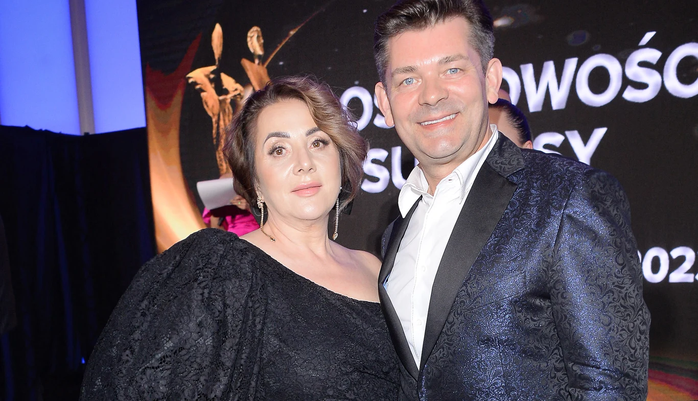 Danuta Martyniuk i Zenon Kobieta i mężczyzna uśmiechają się, pozując razem podczas oficjalnej gali w eleganckich strojach, za nimi widać rozświetlone napisy i elementy scenografii związanej z uroczystością.