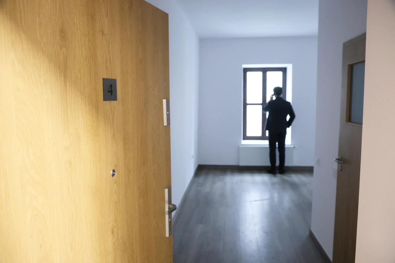 Ulga mieszkaniowa zostanie ograniczona Otwarte drzwi prowadzą do jasnego, pustego pokoju z dużym oknem, przy którym stoi samotna sylwetka mężczyzny patrzącego na zewnątrz.