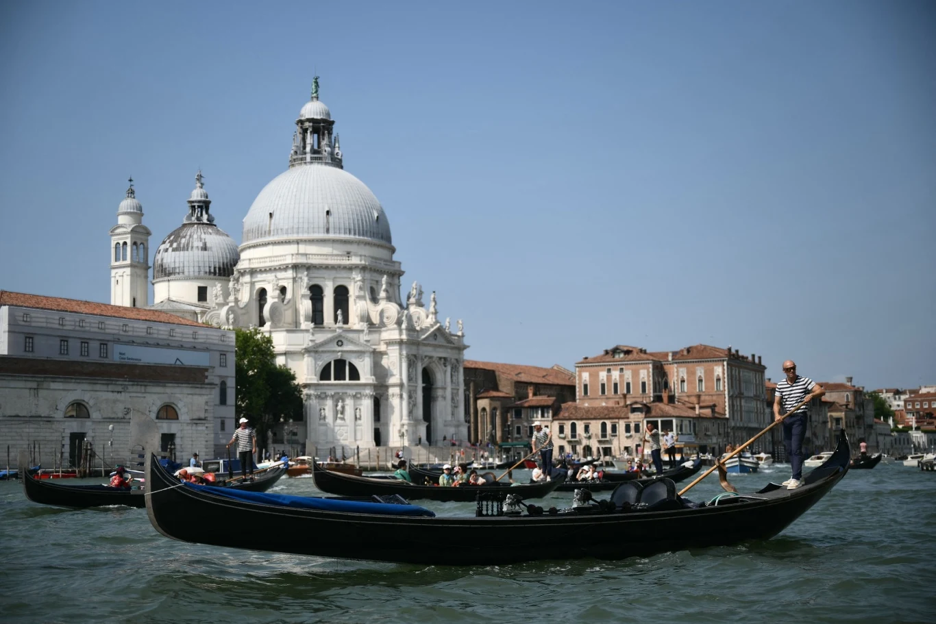 Opłata 100 euro za wstęp do Wenecji - czy pomysł wejdzie w życie? Wenecka gondola płynąca po kanałach, na tle imponującej barokowej bazyliki Santa Maria della Salute, otoczona klasycznymi budynkami i błękitnym niebem.
