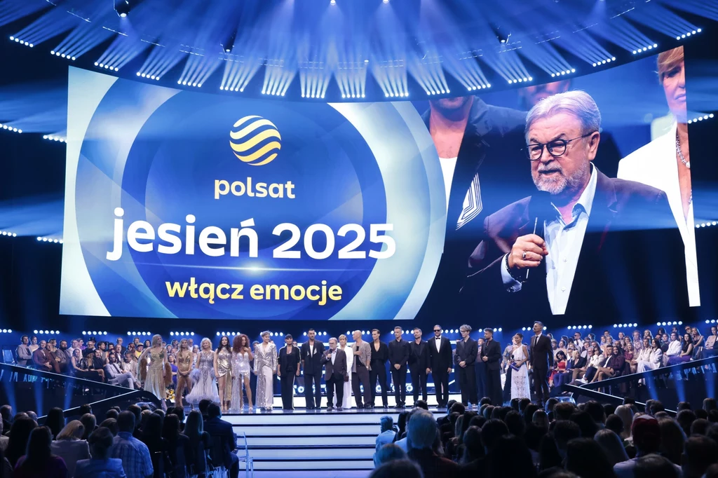 Edward Miszczak podczas prezentacji jesiennej ramówki Polsatu Duża scena telewizyjna z wielkim ekranem, na którym wyświetla się logo Polsatu oraz hasło jesień 2025 włącz emocje, na scenie stoi liczna grupa osób, widownia obserwuje wydarzenie.