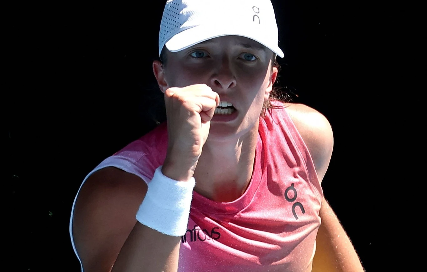 Zbliżenie na skoncentrowaną tenisistkę w białej czapce i różowej koszulce, ściskającą pięść w geście triumfu podczas meczu.