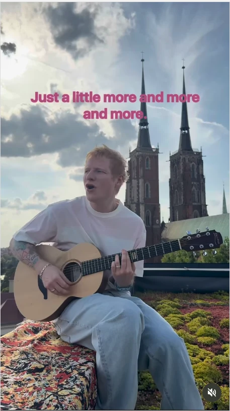 Mężczyzna grający na gitarze akustycznej, siedzący na zewnątrz na tle dwóch gotyckich wież kościelnych, nad nim widoczne fragmenty chmur i napisy z tekstem piosenki.