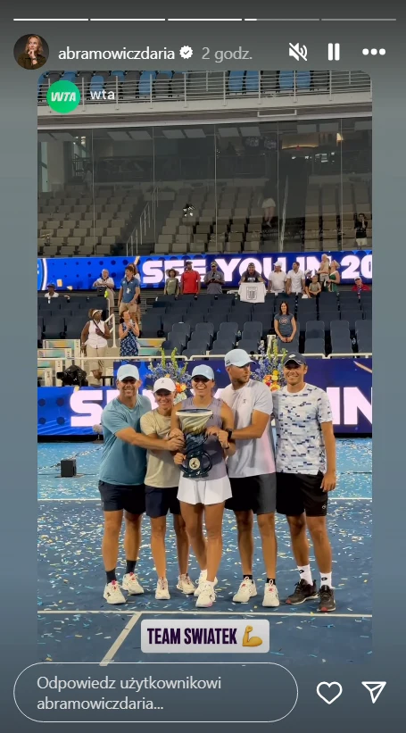 Team Świątek celebruje zwycięstwo Polki Grupa pięciu osób ubranych sportowo stoi razem na korcie tenisowym, obejmując się i trzymając trofeum, w tle widać trybuny oraz duże ekrany z napisem SEE YOU IN 20xx. Wokół leży konfetti, a atmosfera sugeruje sportowy sukces i świętowanie zwycięstwa.