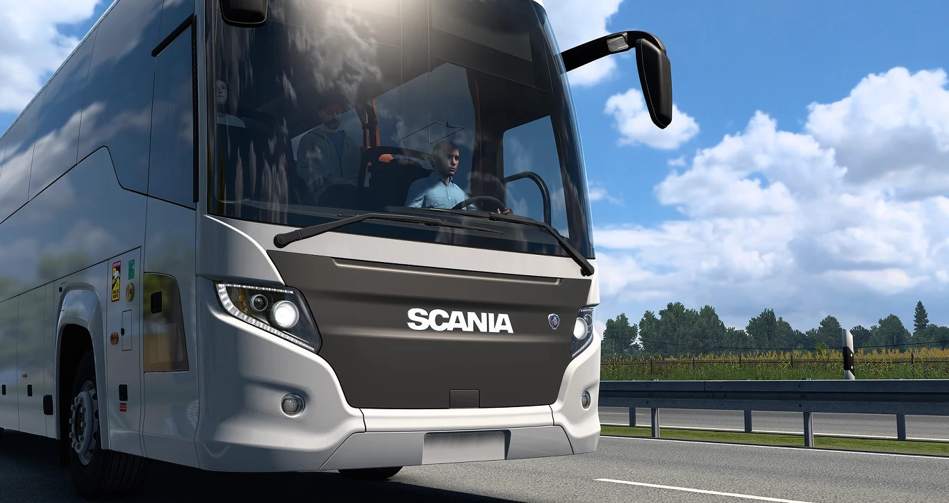 Euro Truck Simulator Autobus marki Scania jadący po autostradzie, widoczny z przodu z wyraźnym logo, w tle błękitne niebo z chmurami oraz fragmenty roślinności przydrożnej.