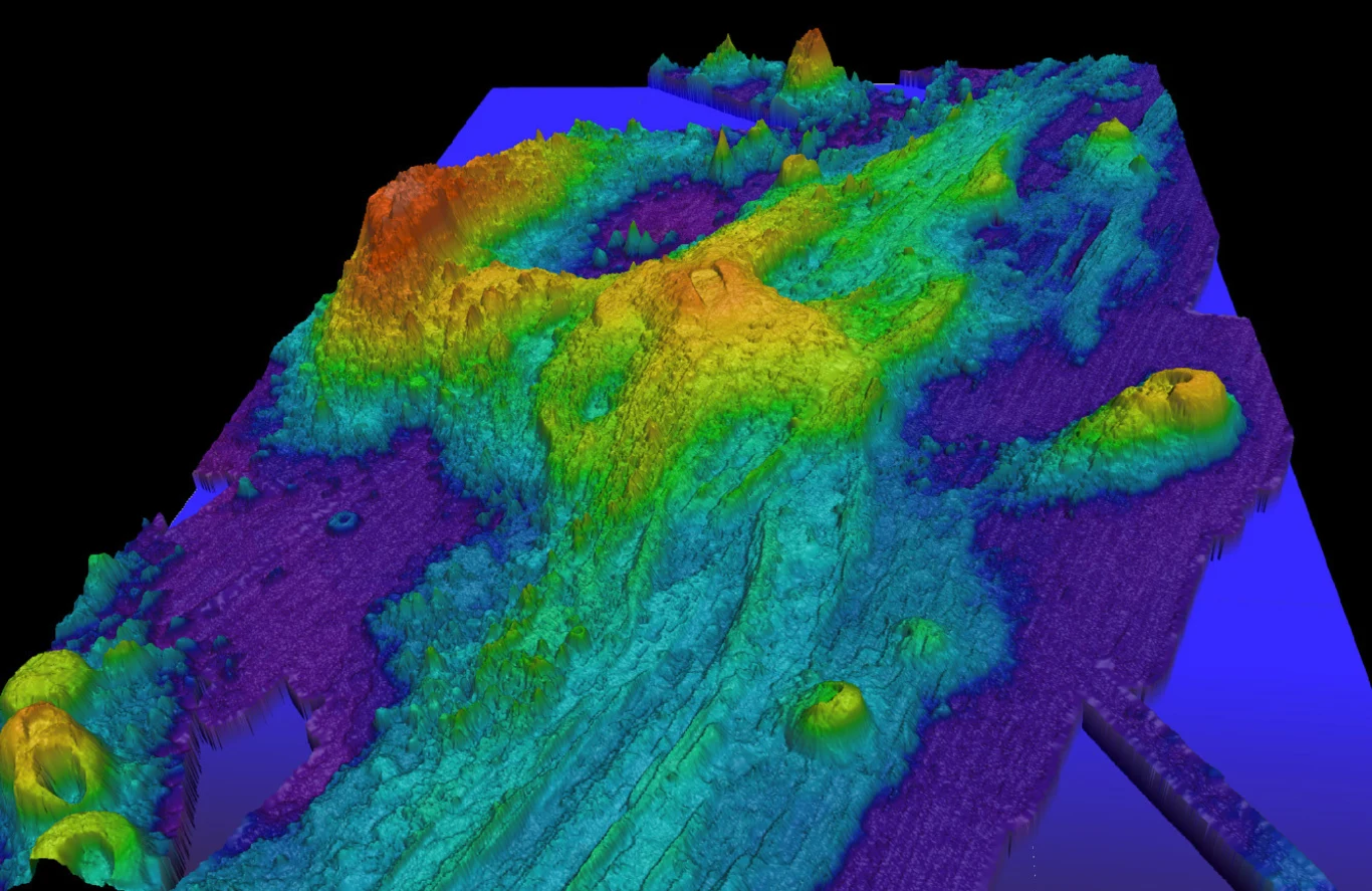 Naukowcy badają Axial Seamonut. To jeden z najlepiej na świecie monitorowanych obszarów dna morskiego. Kolorowa mapa topograficzna przedstawiająca ukształtowanie powierzchni z różnicami wysokości zaznaczonymi gradientem barw od niebieskiego do czerwonego, prawdopodobnie wizualizacja terenu podwodnego lub dna morskiego.