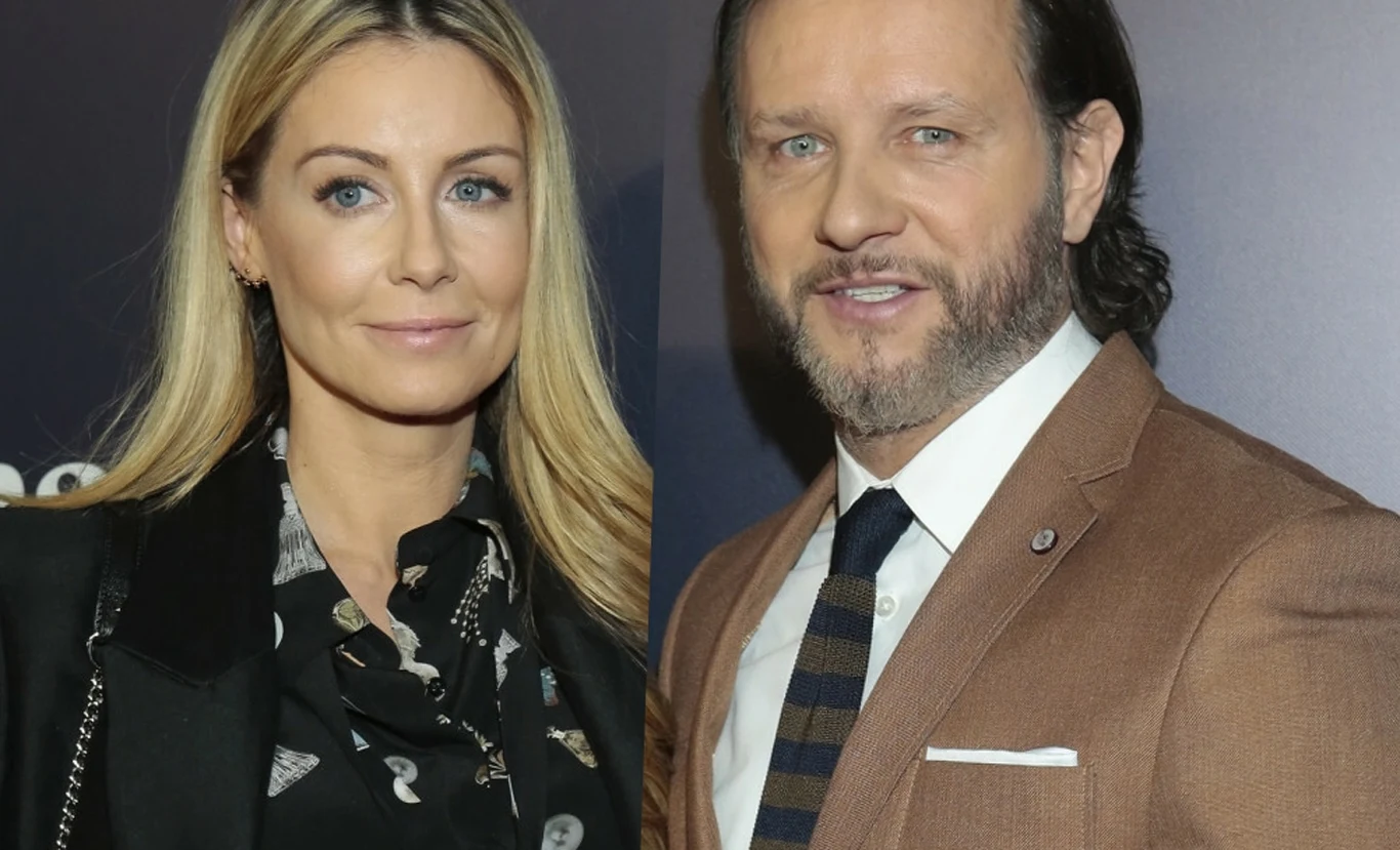 Małgorzata Rozenek-Majdan i Radosław Majdan Kobieta o długich blond włosach i mężczyzna z zarostem, ubrany w brązową marynarkę oraz krawat, stoją obok siebie na tle neutralnej, ciemnej ścianki.