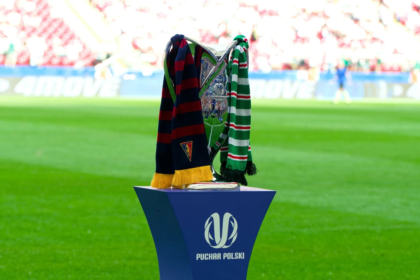 Trofeum Pucharu Polski na stadionie, przystrojone szalikami dwóch drużyn finałowych, w tle rozmyte trybuny i murawa.