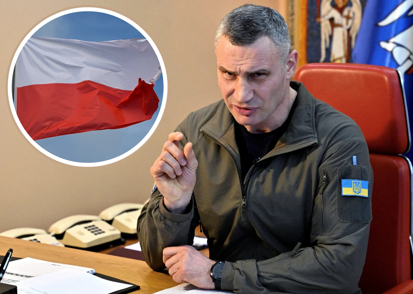 Mężczyzna w wojskowej kurtce z naszywką ukraińskiej flagi siedzi przy biurku, wykonując gest ręką, na tle biura z widocznymi telefonami i religijną ikoną; w okrągłej ramce w lewym górnym rogu znajduje się zdjęcie polskiej flagi.