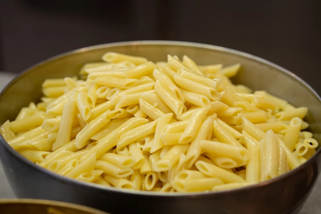Makaron penne Porcja ugotowanego makaronu penne w metalowej misce, jasny kolor makaronu wskazuje na świeżość i prostotę przygotowania dania.