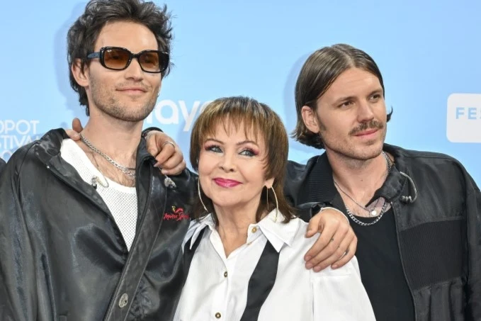 Zespół BEMY (Mattia i Elie Rosinski) z Izabelą Trojanowską podczas Top of the Top Sopot Festival 2025 Troje uśmiechniętych ludzi pozują razem na tle niebieskiej tablicy, dwóch młodszych mężczyzn w ciemnych kurtkach po bokach oraz kobieta w białej koszuli pośrodku, wszyscy w swobodnym i przyjaznym nastroju, z bliskim kontaktem ramion.