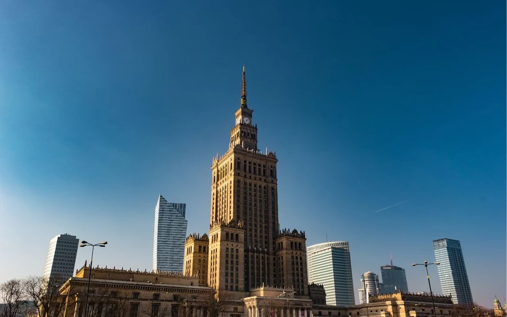 Pałac Kultury i Nauki Pałac Kultury i Nauki w Warszawie otoczony nowoczesnymi wieżowcami, jasne niebo stanowi tło dla miejskiej panoramy.