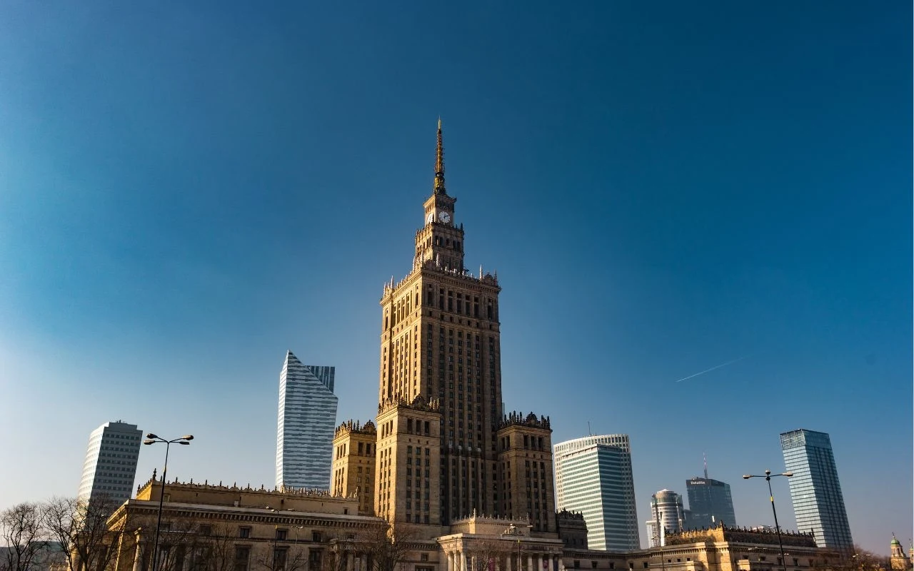 Pałac Kultury i Nauki Pałac Kultury i Nauki w Warszawie otoczony nowoczesnymi wieżowcami, jasne niebo stanowi tło dla miejskiej panoramy.