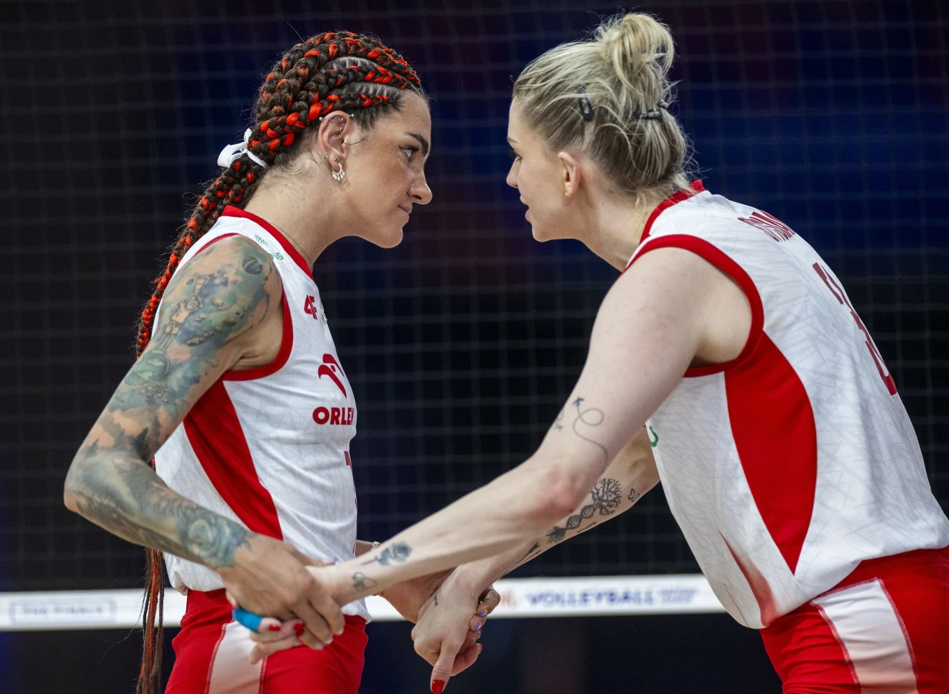 Dwie zawodniczki drużyny siatkarskiej Orlen z poważnymi minami wymieniają gesty w trakcie meczu, w tle widoczna siatka, intensywna atmosfera rywalizacji