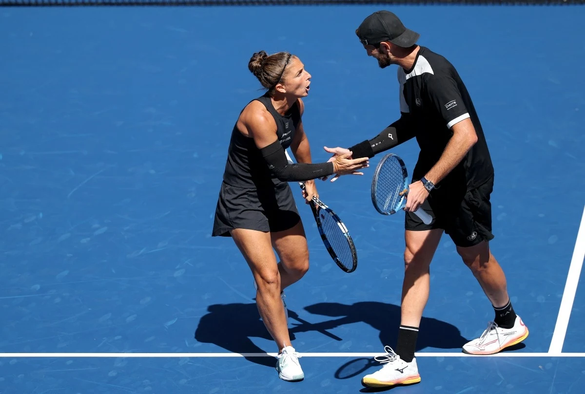 Dwoje tenisistów na korcie w trakcie turnieju, w sportowych strojach, wymieniających między sobą energiczne gesty, trzymając rakiety tenisowe.