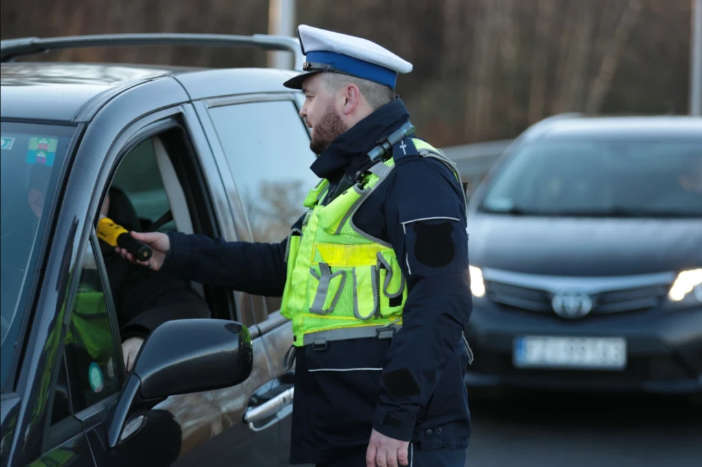 Zerowy limit alkoholu we krwi - obejmie jedną grupę kierowców. Policjant w odblaskowej kamizelce dokonuje kontroli kierowcy używając alkomatu przy otwartym oknie samochodu, w tle widoczny kolejny pojazd oczekujący na swoją kolej.