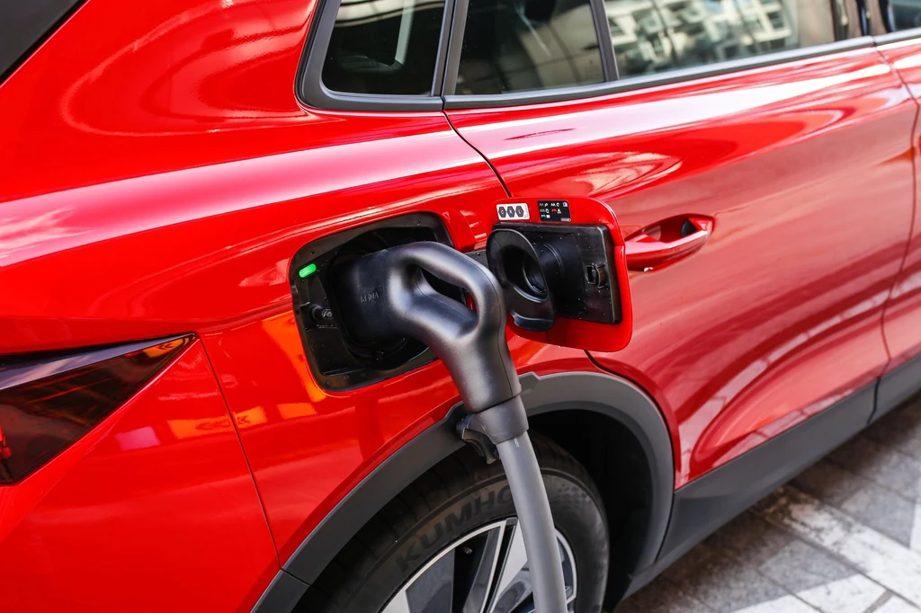 W zależności od wariantu wyposażenia Skoda Elroq może przyjąć prąd stały o mocy do 185 kW. Czerwony samochód elektryczny podczas ładowania, kabel ładowarki podłączony do portu z boku pojazdu, widoczny wyświetlacz z informacjami o postępie.