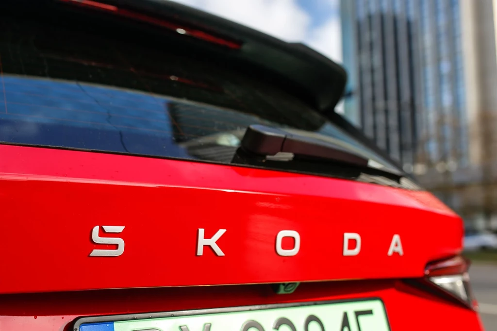 Z tyłu podobnie jak z przodu nie znajdziemy już logo czeskiej marki. Zastąpił ją napis "SKODA". Czerwony samochód osobowy marki Škoda, ujęcie z tyłu eksponujące logo producenta i fragment tablicy rejestracyjnej, w tle rozmyte wysokie budynki.
