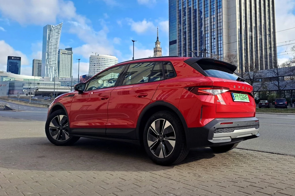 Zgodnie z ceną katalogową Skoda Elroq kosztuje co najmniej 149 900 zł. Czerwony samochód osobowy SUV marki Skoda zaparkowany na tle nowoczesnej zabudowy miejskiej z wysokimi wieżowcami i charakterystycznym Pałacem Kultury i Nauki w Warszawie.