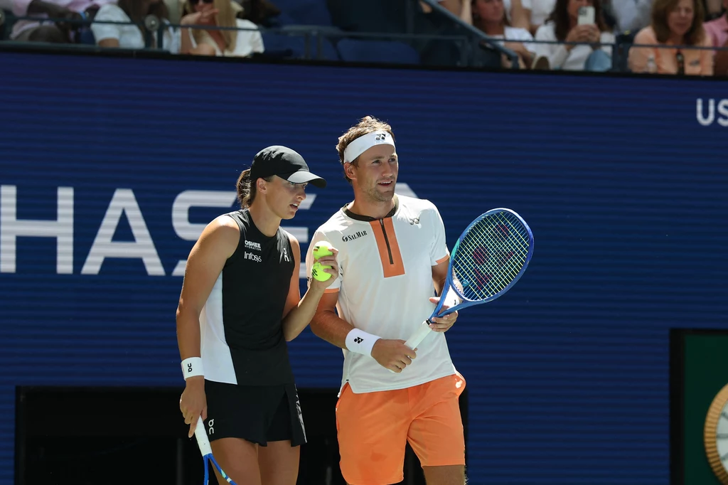 Iga Świątek i Casper Ruud w trakcie turnieju miksta US Open 2025 Dwoje tenisistów ubranych w sportowe stroje rozmawia ze sobą na korcie podczas turnieju, trzymając rakiety oraz piłkę tenisową, w tle widoczni kibice na trybunach.