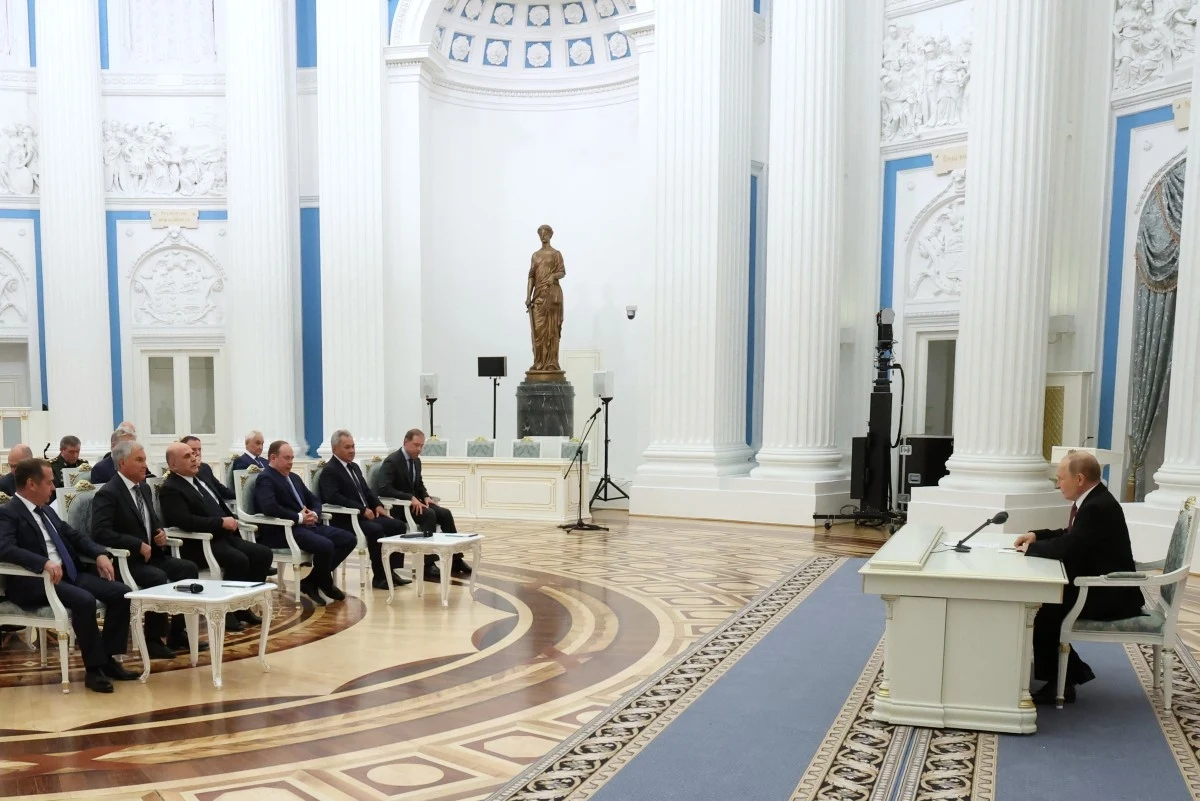 Spotkanie wysokich rangą urzędników w okazałej sali z marmurowymi kolumnami, dużą rzeźbą i eleganckimi fotelami, gdzie jedna osoba siedzi przy biurku, a reszta w rzędzie naprzeciwko.