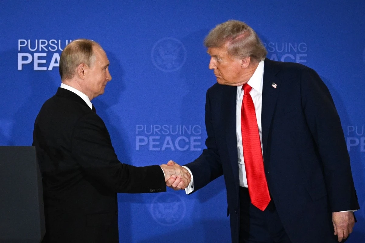 Dwóch mężczyzn w garniturach wymienia uścisk dłoni na tle niebieskiego ekranu z napisem 'Pursuing Peace', jeden z nich ma czerwoną krawat, drugi czarną.