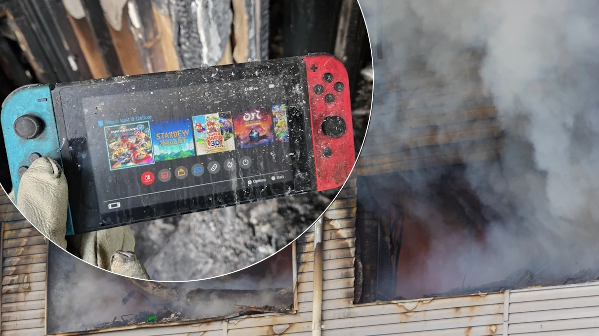 Czy cudowne ocalenie konsola Nintendo zawdzięcza zwykłemu szczęściu czy może stacji dokującej? Tego już się nie dowiemy Ręka w rękawicy ochronnej trzyma konsolę Nintendo Switch pokrytą osadem po pożarze, a w tle widoczne są spalony budynek oraz unoszący się dym.