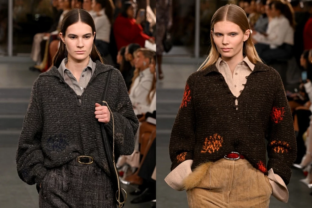Tory Burch jesień/zima 2025-2026 Dwie modelki prezentujące stylizacje z kolekcji jesienno-zimowej, obie ubrane w grube swetry z kołnierzykami i spodnie z wysokim stanem, w tle publiczność siedząca na trybunach.