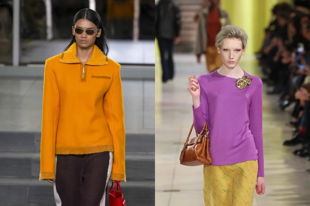 Tory Burch, Miu Miu jesień/zima 2025-2026. Fot. Victor VIRGILE ,Victor Boyko Dwie modelki prezentujące najnowsze trendy mody, jedna ubrana w żółty golf z długim rękawem, ciemne spodnie i okulary przeciwsłoneczne, druga w fioletowy sweter z broszką, żółtą spódnicę i trzymająca brązową torebkę, idące po wybiegu otoczonym przez pu...