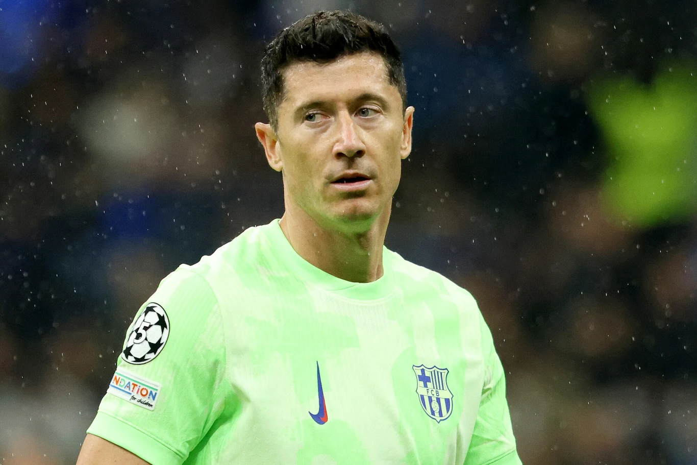 Piłkarz w jasnej, seledynowej koszulce klubu FC Barcelona, z logo Ligi Mistrzów na rękawie, znajduje się na murawie stadionu, tło jest rozmyte.