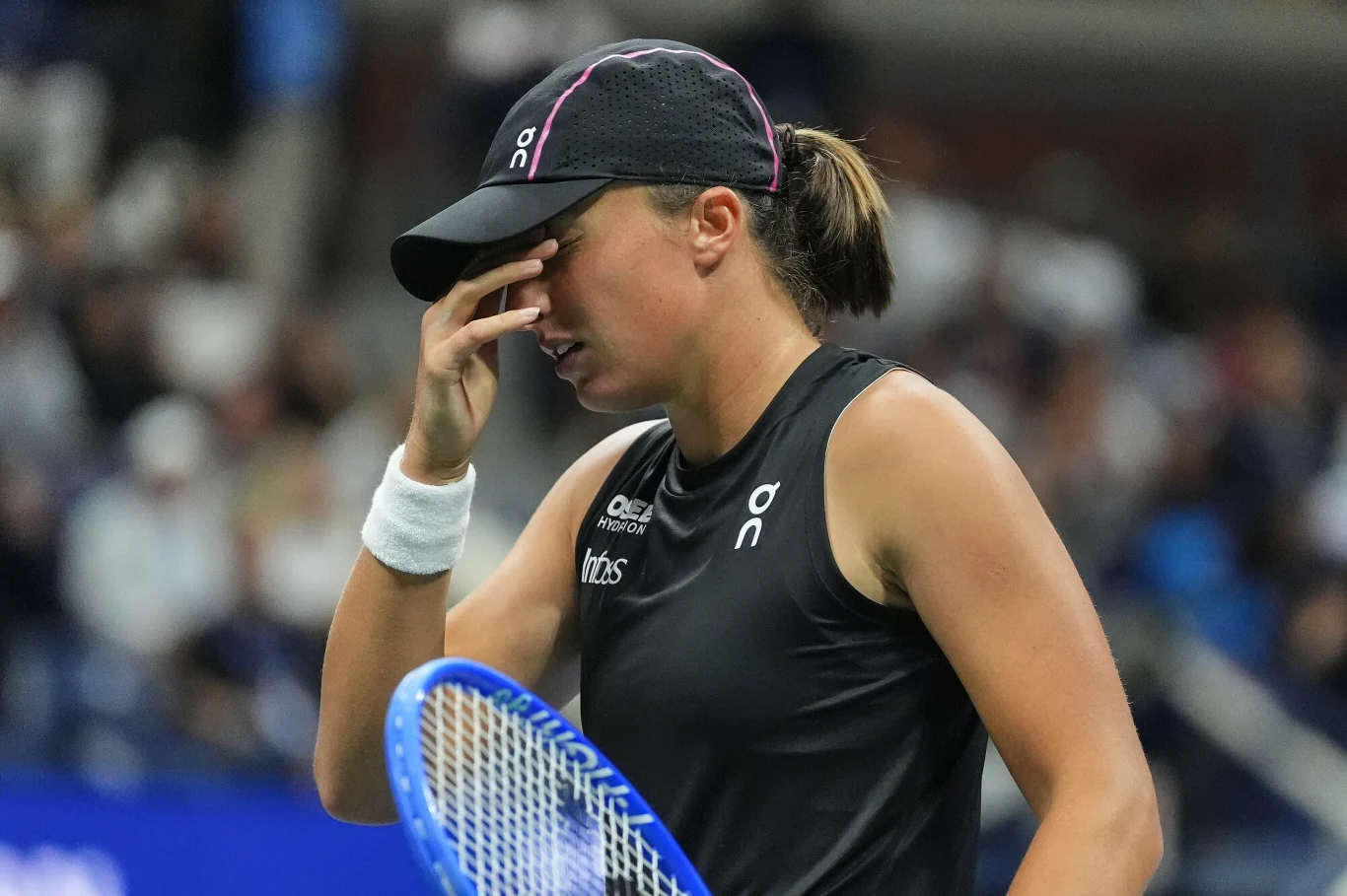Iga Świątek podczas finału miksta na US Open Tenisistka w czarnej koszulce i czapce z daszkiem stoi na korcie, trzyma rakietę w jednej ręce i zakrywa twarz drugą dłonią, wyrażając emocje po meczu.